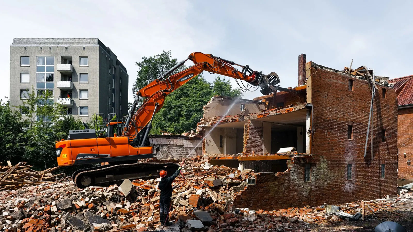 Ein Bagger bricht ein Backsteingebäude ab, davor liegt Bauschutt.